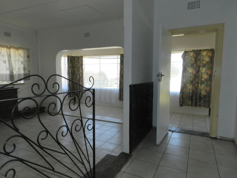 An empty living area featuring tiled flooring, a decorative wrought iron balustrade, and an arched transition leading to an adjacent room.