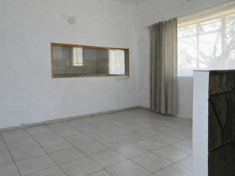 An empty living room featuring tiled flooring, a decorative stone feature wall, and a serving hatch connecting to the kitchen area.