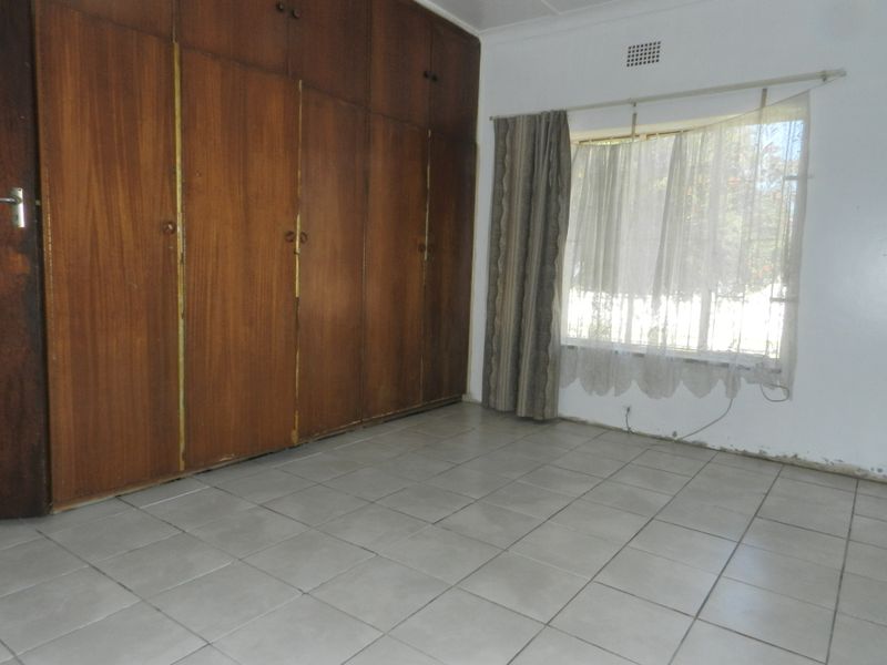 An empty bedroom featuring tiled flooring and extensive built-in wooden cupboards, offering a blank canvas for renovation and modernization.