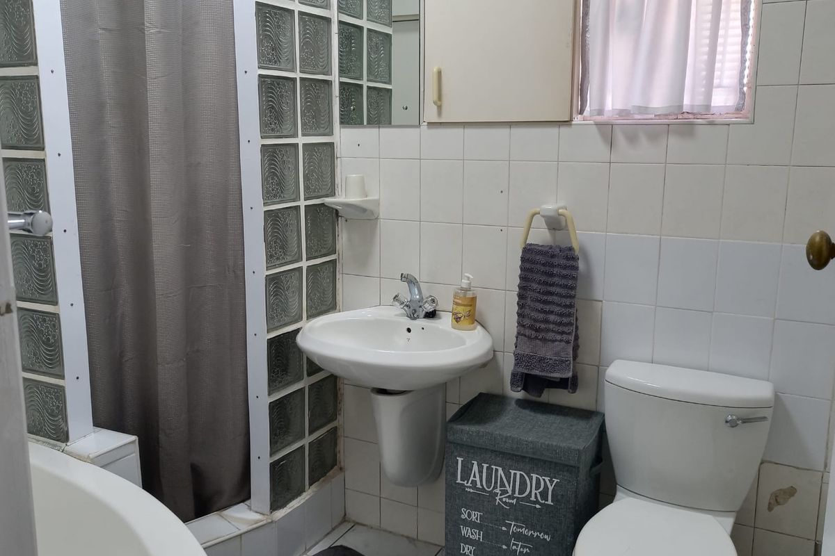A dated bathroom featuring a pedestal sink, glass block shower partition, and ceramic wall tiling, requiring cosmetic updates to modernize the space.