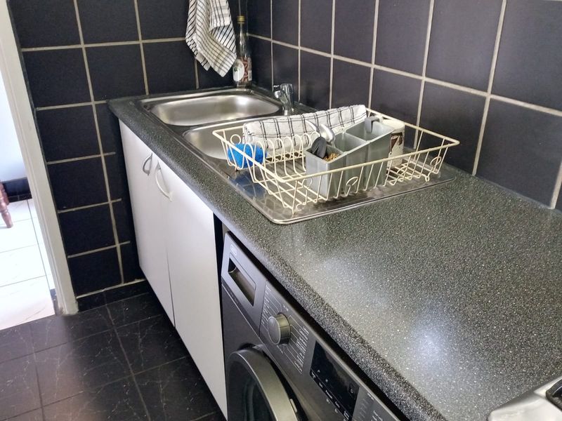 A functional laundry area featuring a stainless steel sink, laminate countertop, built-in cabinetry, and dark tiled finishes.