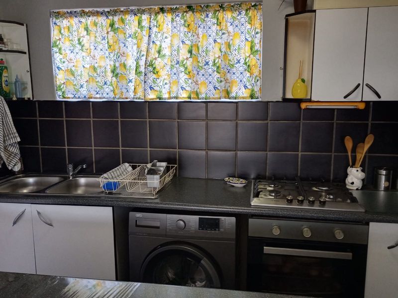 A functional kitchen featuring dark tiled backsplash, built-in cabinetry, gas hob, oven, and an integrated washing machine.