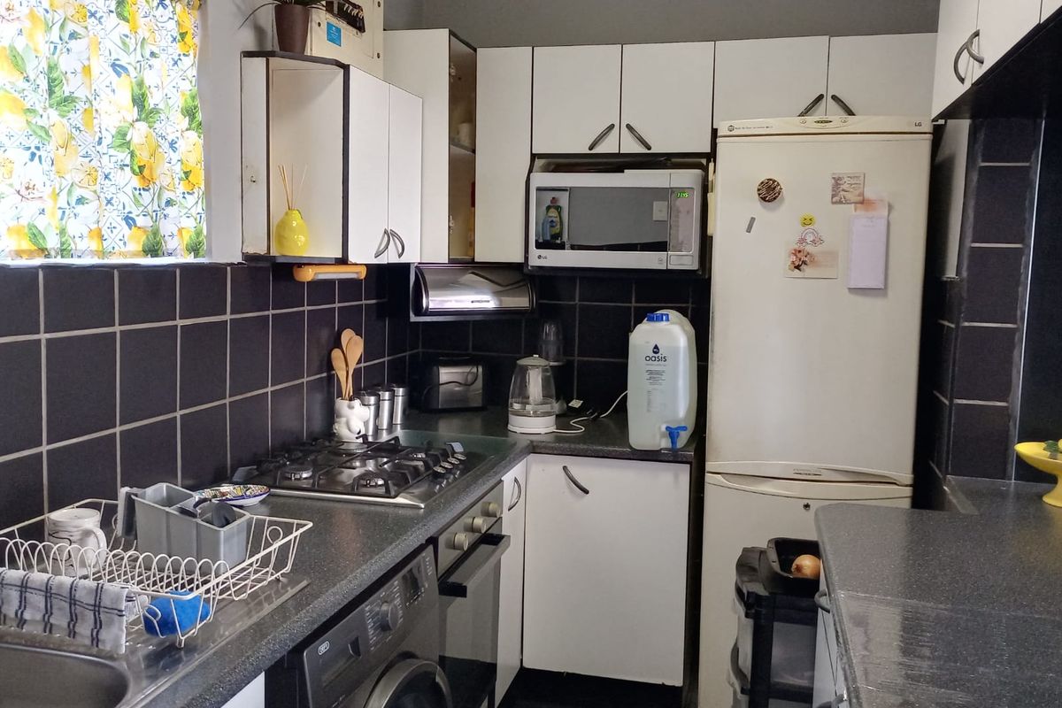 Compact kitchen featuring a gas hob, built-in oven, microwave, laminate countertops, and dark tiled backsplash with ample upper and lower cabinetry storage.