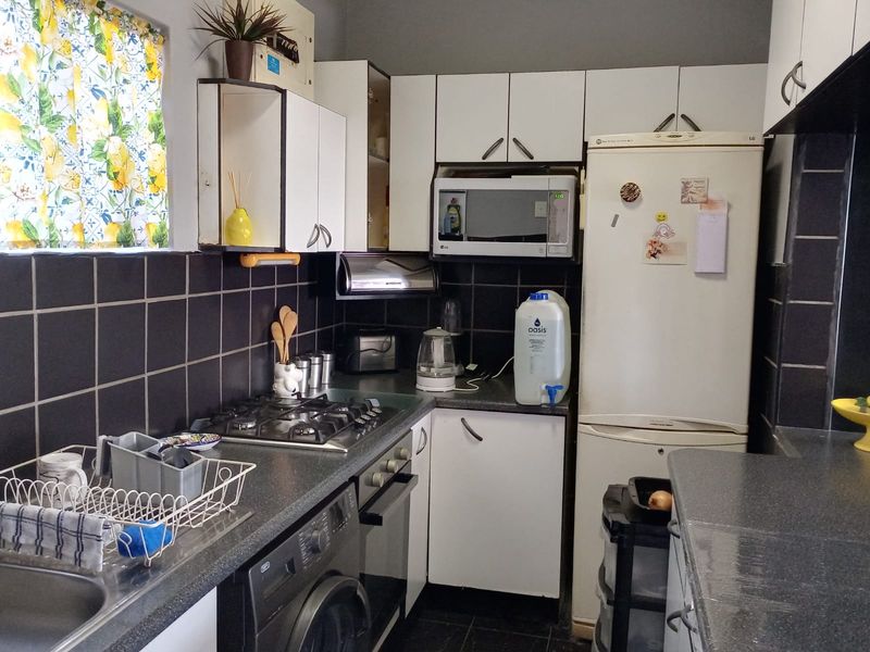 Compact kitchen featuring a gas hob, built-in oven, microwave, laminate countertops, and dark tiled backsplash with ample upper and lower cabinetry storage.