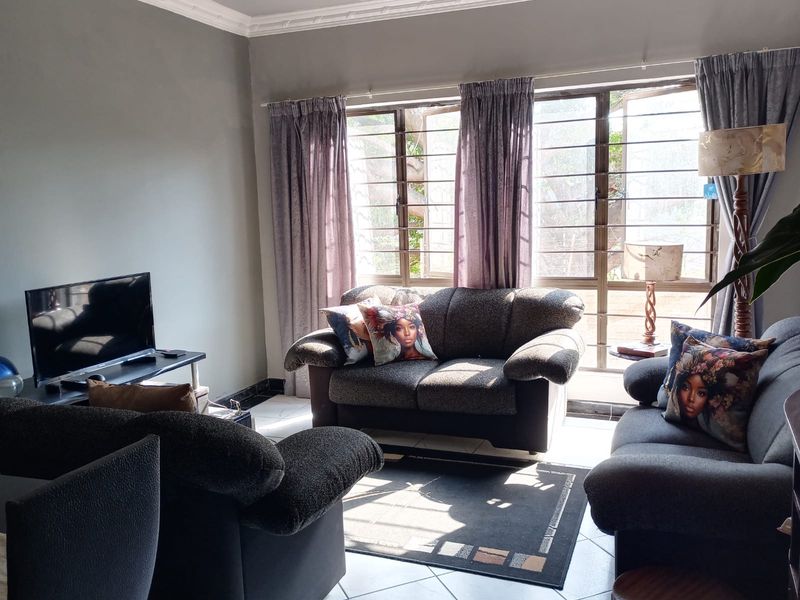 A comfortable living room featuring tiled flooring, large windows with security bars, and decorative ceiling cornicing, providing a bright and functional space.