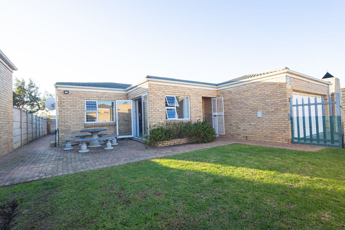 Rear view of the property featuring a face brick facade, paved patio area, and a well-maintained lawn.