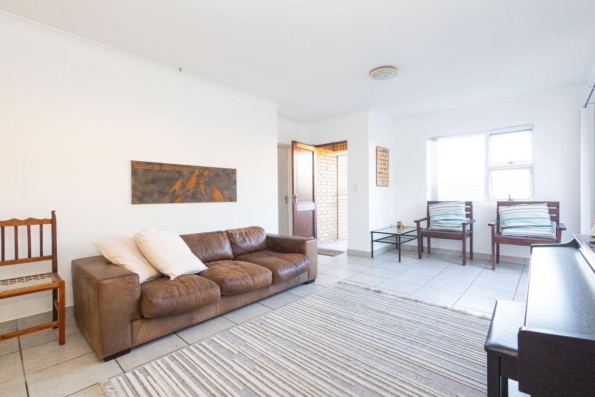 A bright living room featuring neutral tiled flooring, white walls, and a large window allowing for natural light.