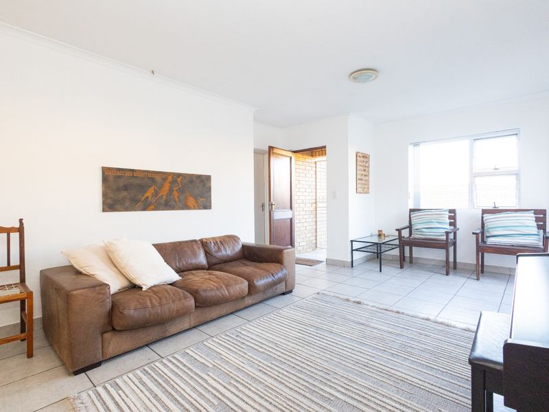 A bright living room featuring neutral tiled flooring, white walls, and a large window allowing for natural light.