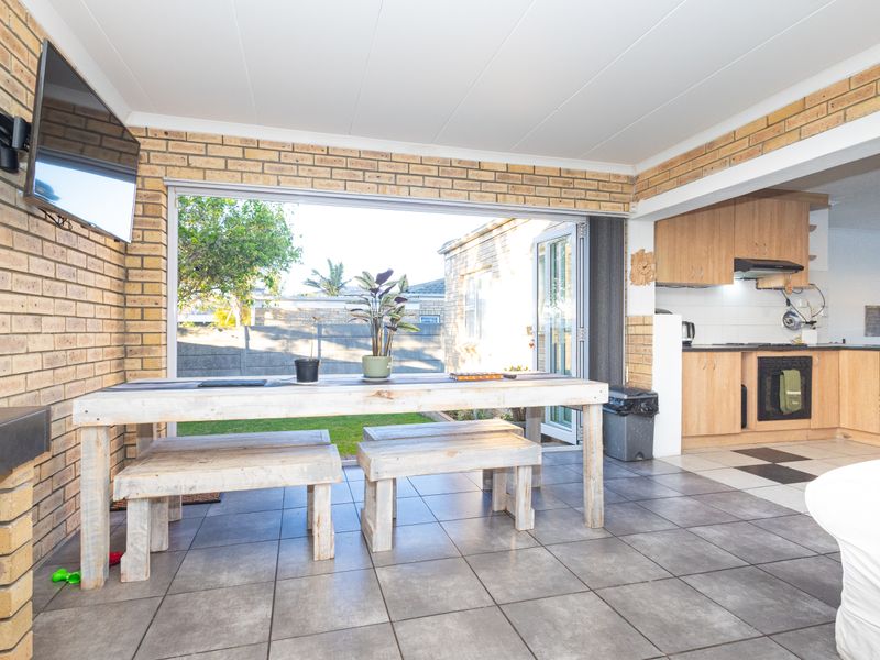 Open-plan living and kitchen area featuring exposed brick walls, tiled flooring, and direct access to the garden through large sliding glass doors.
