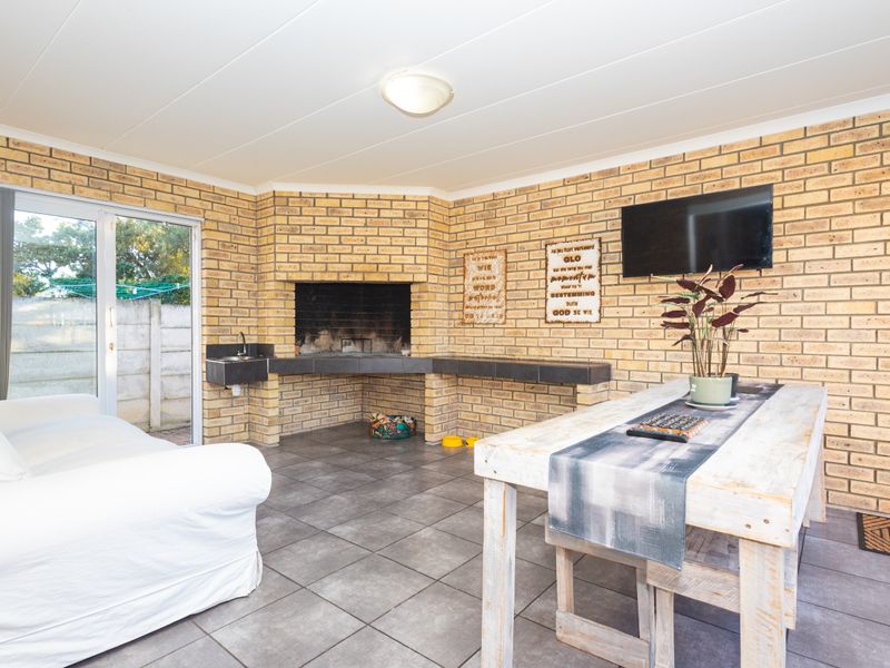 Enclosed patio area featuring a built-in brick braai, tiled flooring, and direct access to the garden through sliding glass doors.