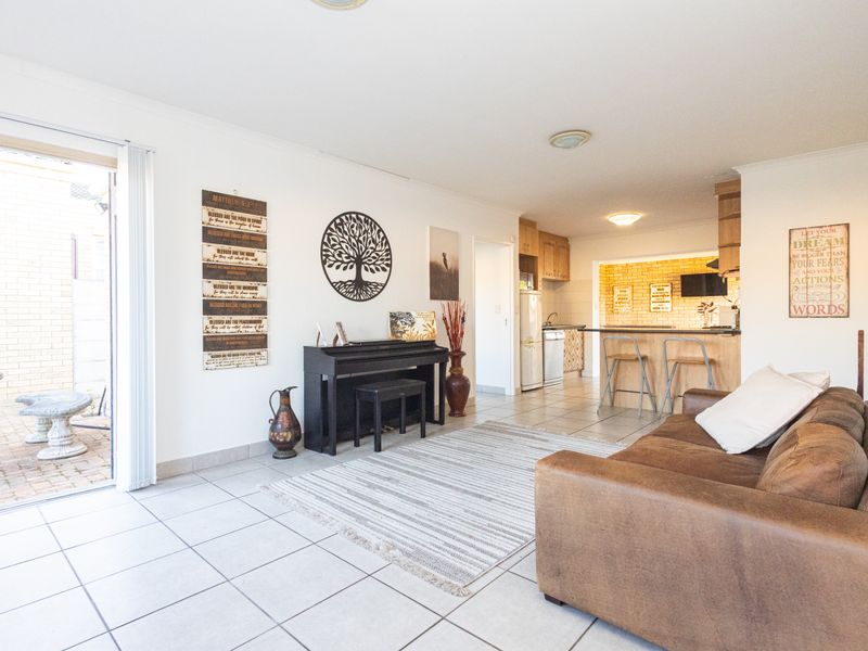 Open-plan living area featuring tiled flooring, a breakfast bar kitchen, and direct access to an outdoor patio through sliding glass doors.