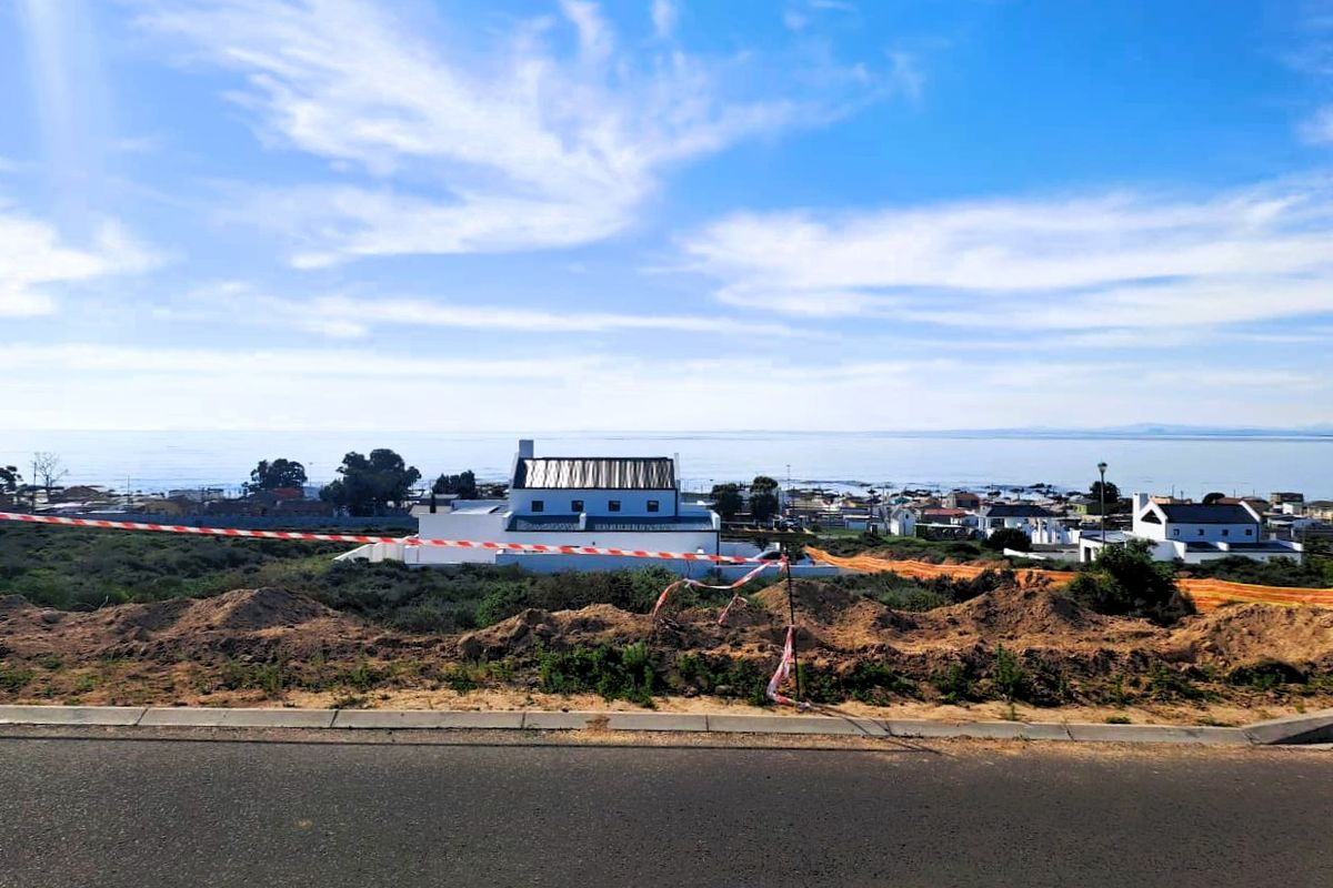 A scenic view overlooking a coastal residential area with ocean vistas, captured from an elevated position near a road.