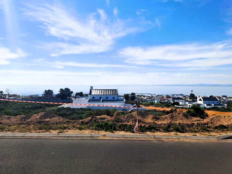 A scenic view overlooking a coastal residential area with ocean vistas, captured from an elevated position near a road.