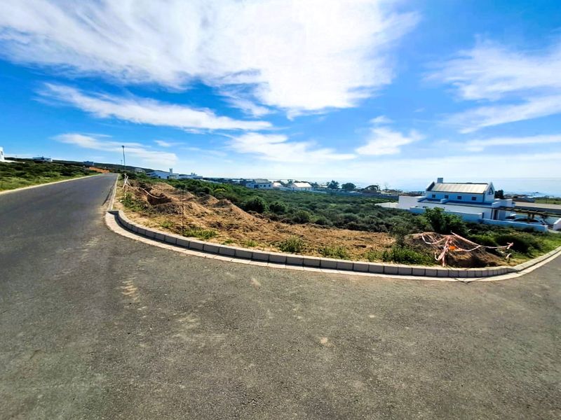 A view of a vacant residential plot situated on a corner lot, featuring established concrete curbing and access to a paved road.