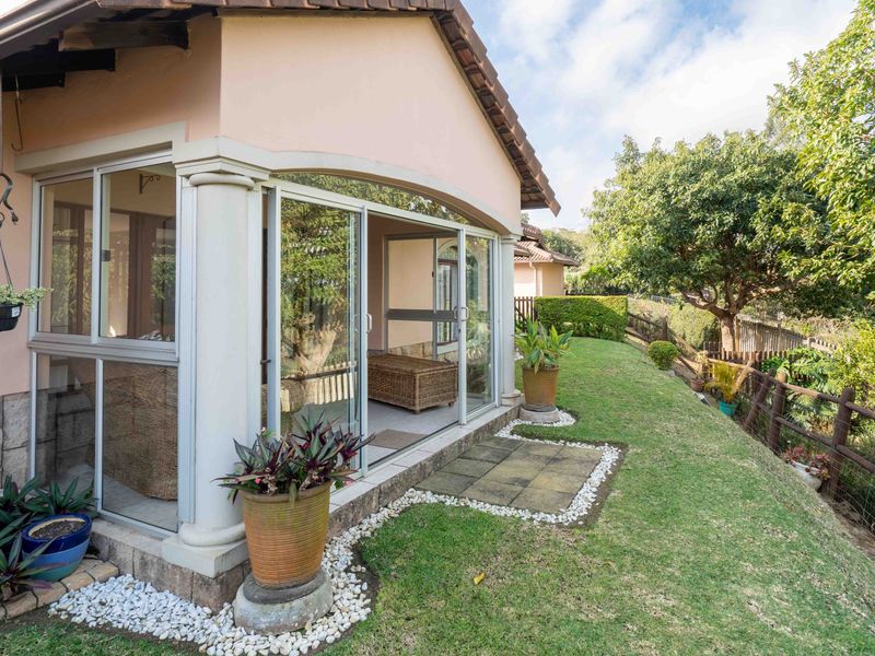 A covered patio area featuring sliding glass doors, stone cladding, and decorative columns, overlooking a well-maintained garden space.