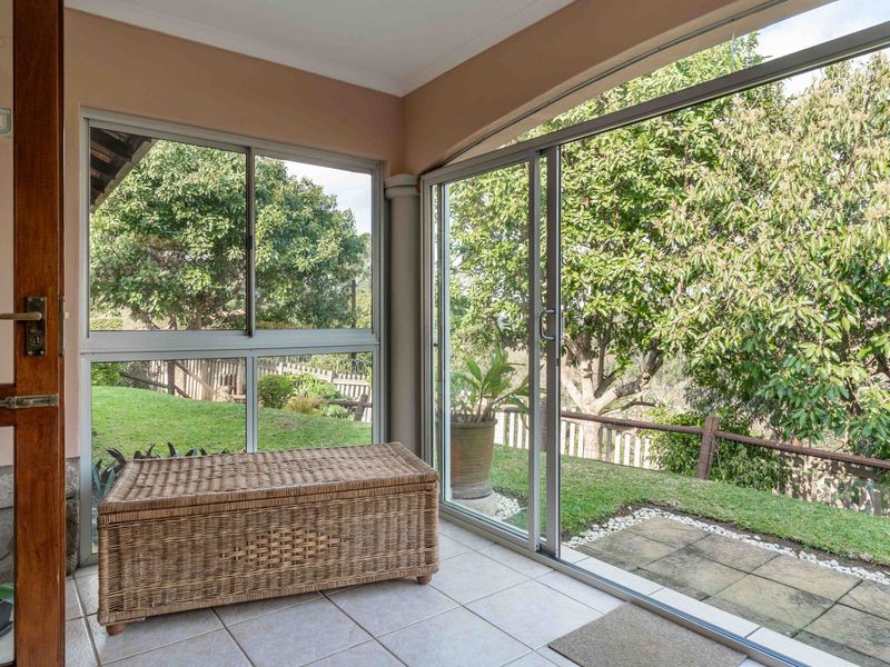 A bright, enclosed patio area featuring tiled flooring and large sliding glass doors that provide direct access to the garden.