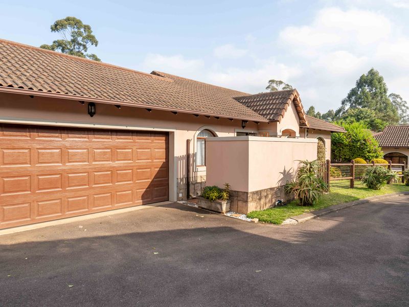 Front exterior view of the townhouse featuring a paved driveway, a secure garage door, and a well-maintained masonry boundary wall.