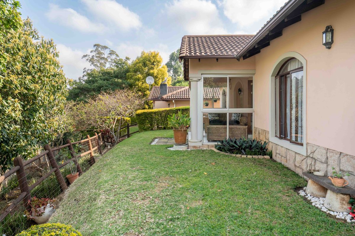 A well-maintained rear garden area featuring a lawn, stone-clad exterior wall, and an enclosed patio space with a tiled roof.