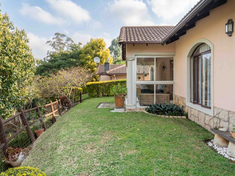 A well-maintained rear garden area featuring a lawn, stone-clad exterior wall, and an enclosed patio space with a tiled roof.