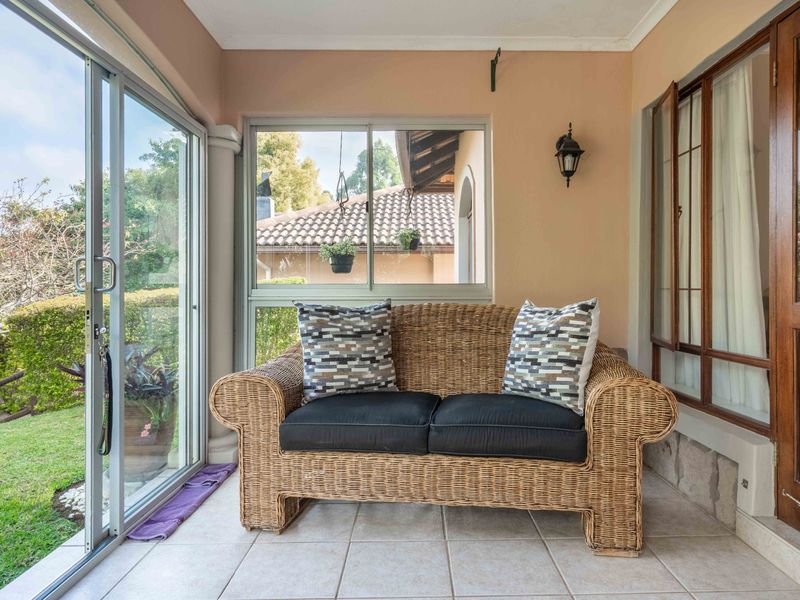 A covered patio area featuring tiled flooring, sliding glass doors leading to the garden, and large windows providing natural light.