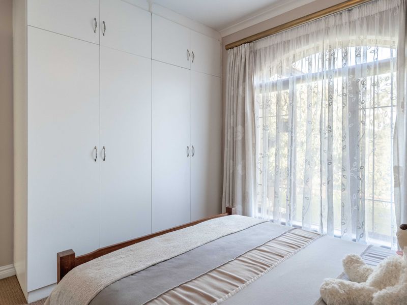 A well-maintained bedroom featuring floor-to-ceiling built-in cupboards and a large arched window with natural light.