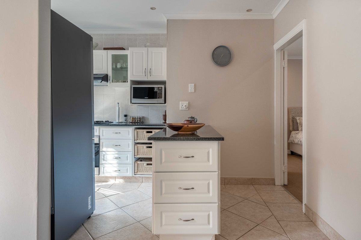 A well-maintained kitchen featuring white cabinetry, granite countertops, a central island, and tiled flooring, with a seamless transition to the adjacent room.