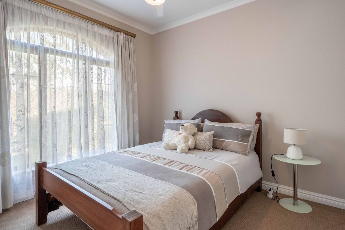 A well-maintained bedroom featuring neutral wall tones, carpeted flooring, and a large arched window that allows for ample natural light.