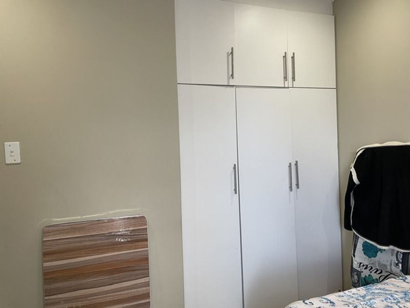 A bedroom featuring a white built-in wardrobe with integrated overhead storage cupboards.
