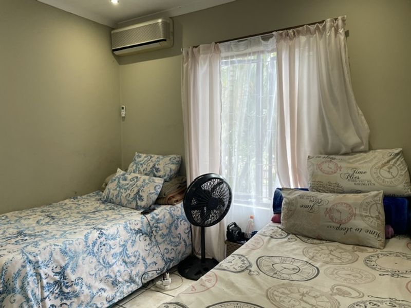 A bedroom featuring tiled flooring, a wall-mounted air conditioning unit, and a window fitted with security bars.