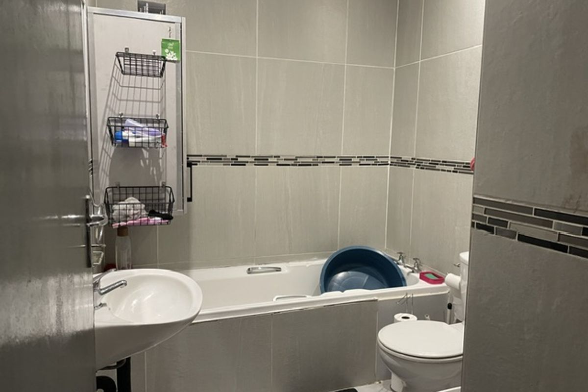 A functional bathroom featuring a bathtub, pedestal basin, and toilet with neutral wall tiling and a decorative mosaic border.