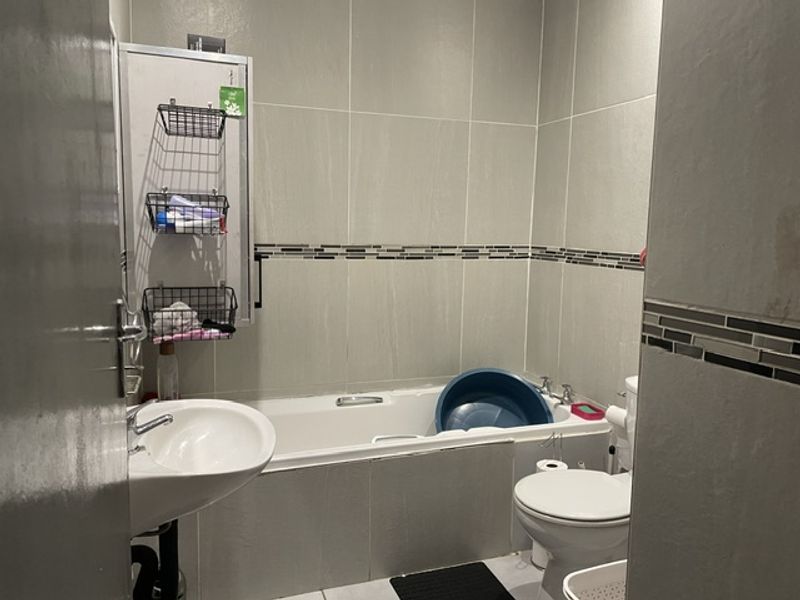 A functional bathroom featuring a bathtub, pedestal basin, and toilet with neutral wall tiling and a decorative mosaic border.