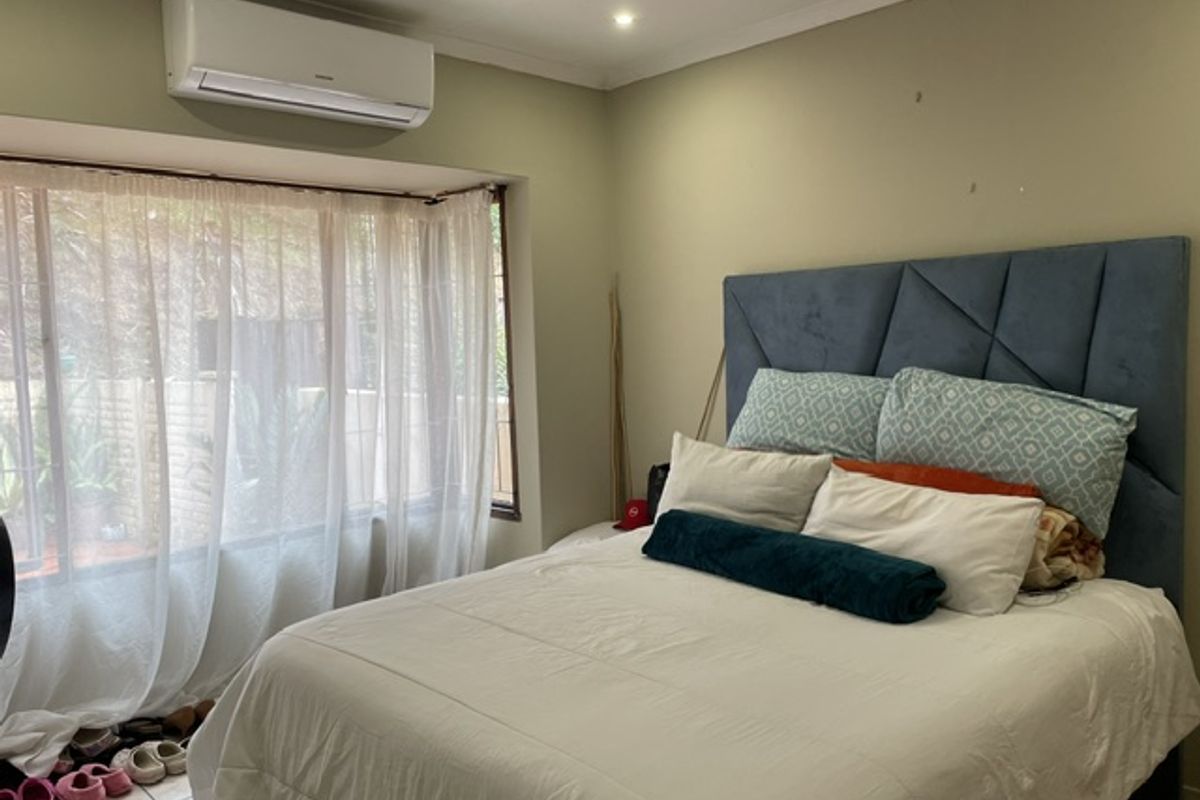A bedroom featuring tiled flooring, a wall-mounted split-system air conditioner, and large windows with natural light.