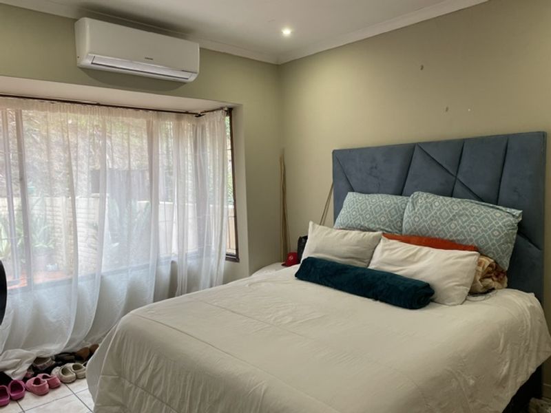A bedroom featuring tiled flooring, a wall-mounted split-system air conditioner, and large windows with natural light.