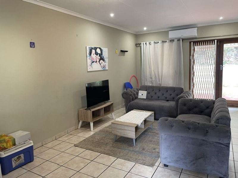 A living room featuring tiled flooring, recessed downlights, and a wall-mounted air conditioning unit, with direct access to an outdoor area via a sliding door.
