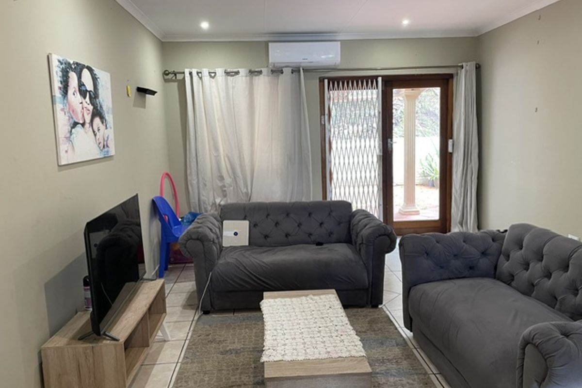 A comfortable living room featuring tiled flooring, a wall-mounted air conditioning unit, and direct access to an outdoor area through a secure sliding door.