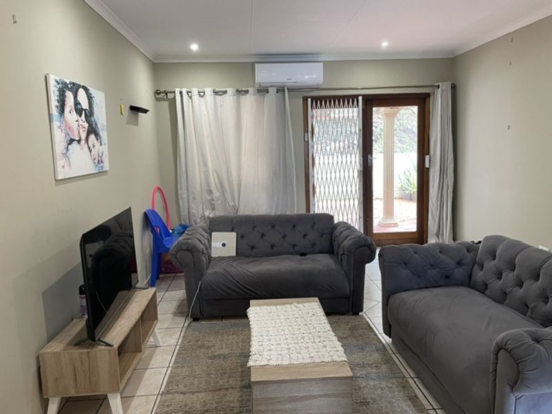 A comfortable living room featuring tiled flooring, a wall-mounted air conditioning unit, and direct access to an outdoor area through a secure sliding door.