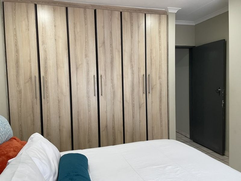 A well-maintained bedroom featuring extensive floor-to-ceiling built-in wooden cupboards and a neutral interior finish.