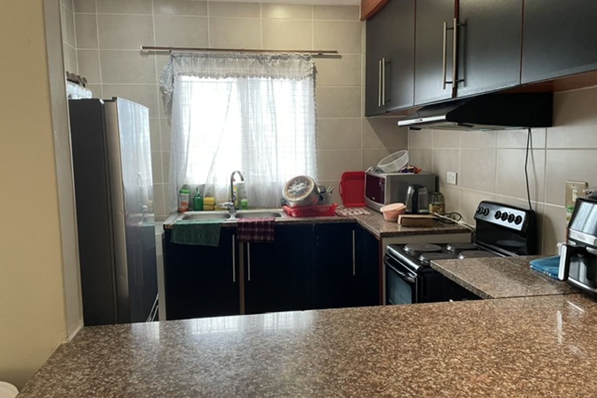 A functional kitchen featuring dark cabinetry, granite countertops, a tiled backsplash, and integrated appliances including an electric stove and extractor fan.