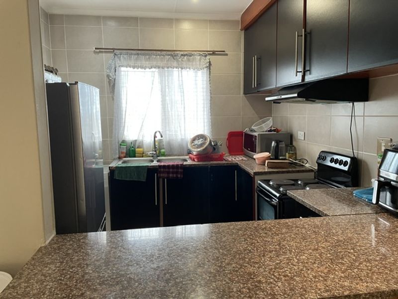 A functional kitchen featuring dark cabinetry, granite countertops, a tiled backsplash, and integrated appliances including an electric stove and extractor fan.