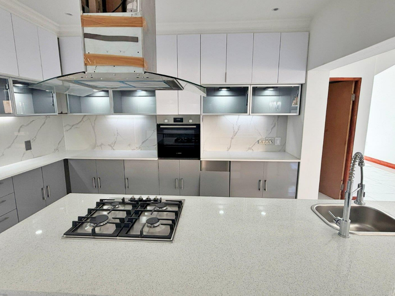 Modern kitchen featuring a central island with a gas hob and sink, complemented by sleek cabinetry, quartz countertops, and a marble-look splashback.