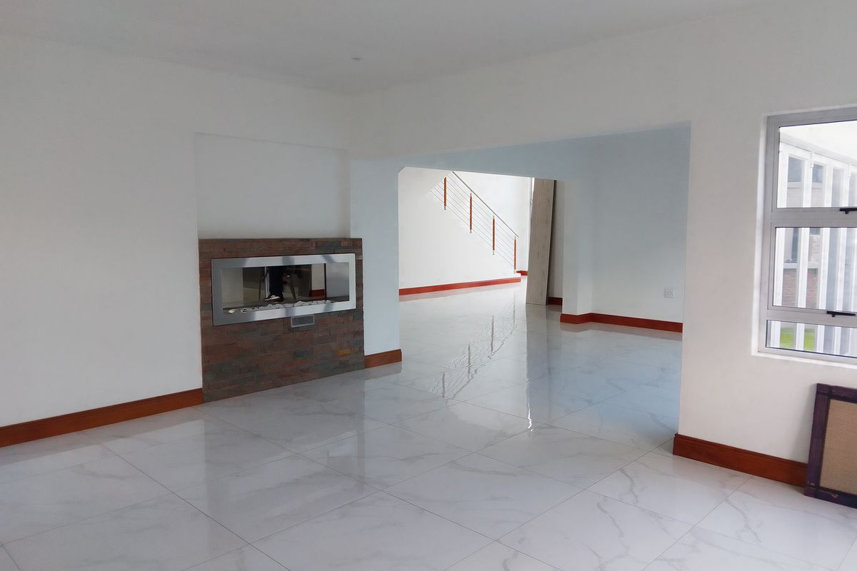 Spacious open-plan living area featuring polished marble-look floor tiles, a modern built-in fireplace with stone cladding, and a view toward the staircase.