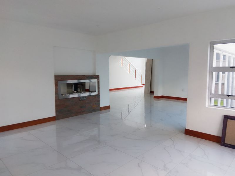 Spacious open-plan living area featuring polished marble-look floor tiles, a modern built-in fireplace with stone cladding, and a view toward the staircase.