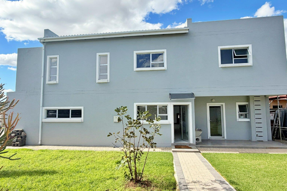 Rear view of a modern two-story house featuring a grey rendered facade, paved walkway, and well-maintained lawn.