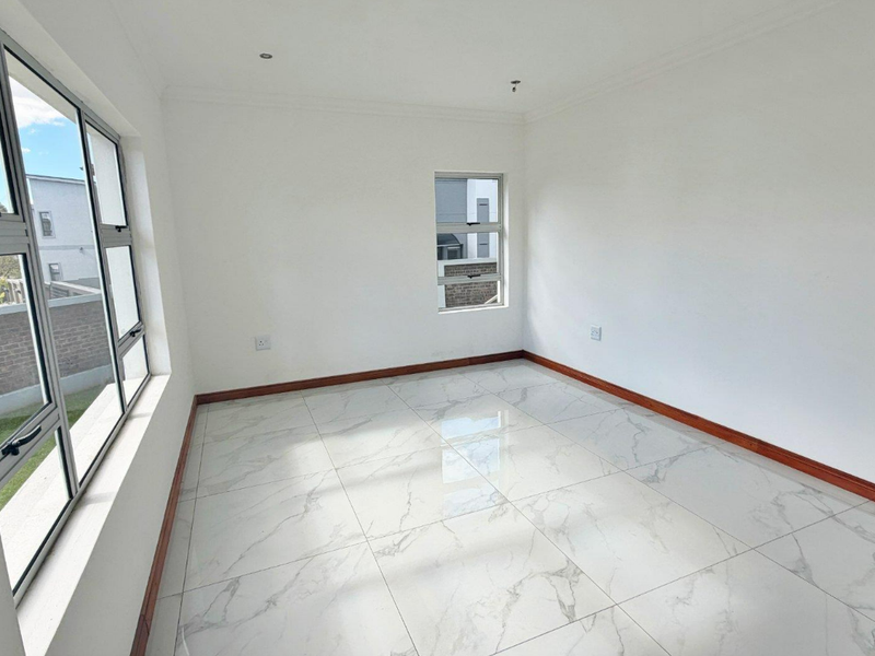 A bright, empty bedroom featuring modern marble-look floor tiles, white walls, and aluminium-framed windows.