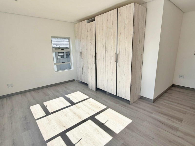 A bright, empty bedroom featuring modern light wood-grain built-in cupboards and matching laminate flooring.