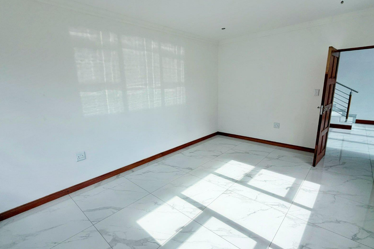 A bright, empty bedroom featuring modern marble-look floor tiles, wooden skirting boards, and a timber door leading to a hallway.