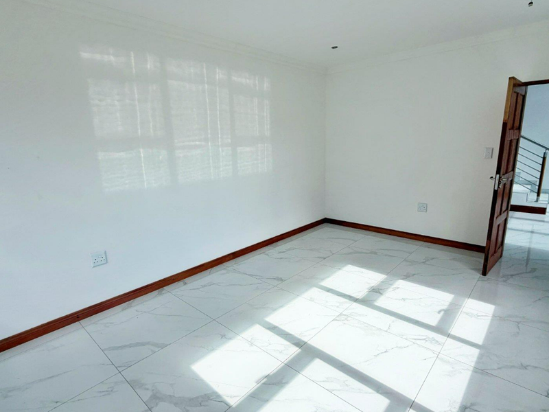 A bright, empty bedroom featuring modern marble-look floor tiles, wooden skirting boards, and a timber door leading to a hallway.