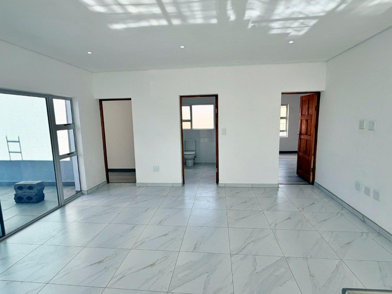 A bright, empty living area featuring modern marble-look floor tiles, recessed lighting, and large sliding glass doors leading to an outdoor balcony.