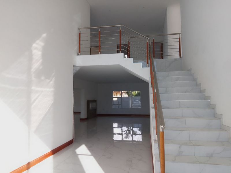 Spacious entrance hall featuring a modern tiled staircase with a stainless steel and wood balustrade, leading to an open mezzanine landing.