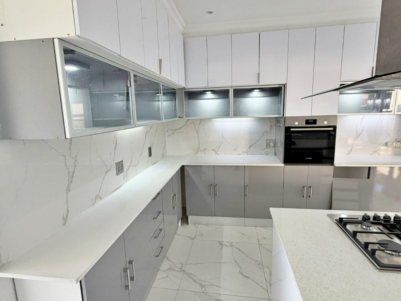 Modern kitchen featuring two-tone cabinetry, marble-look splashbacks, stone countertops, built-in oven, and a gas cooktop on the central island.